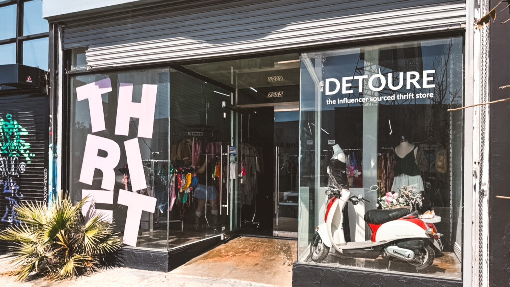 The front of the Detoure store with clothing and mannequins in the windows and THRIFT in big, light pink letters on the window.
