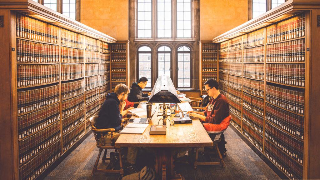 Students sit at a table surrounded by bookshelves as they study for finals in the Law Library of Myron Taylor Hall