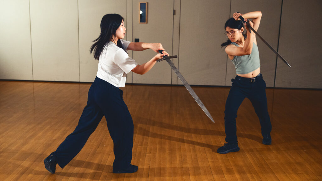 Two students performing a fight with swords.