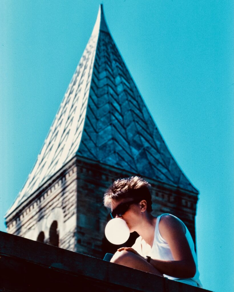 a student studying outside blows a bubble with McGraw Tower in the background in spring 1985