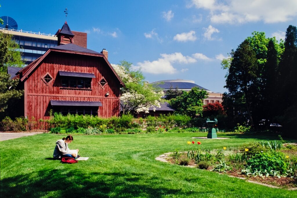 a student studies on the lawn behind the Big Red Barn and by the gardens behind the A.D. White House in spring 1999