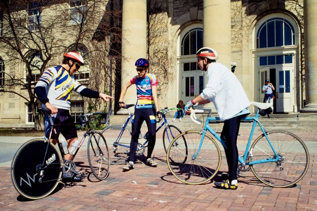 three cyclists chat and compare bikes in front of Goldwin Smith Hall in spring 1992