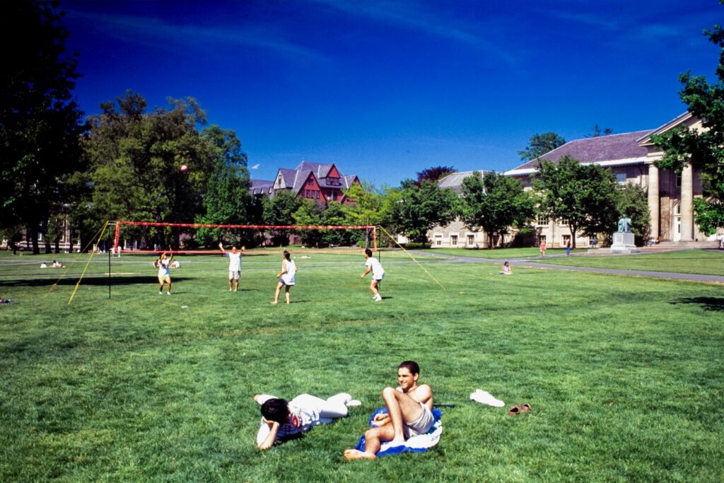 students relax in the grass as others play volleyball on the Arts Quad in spring 1992