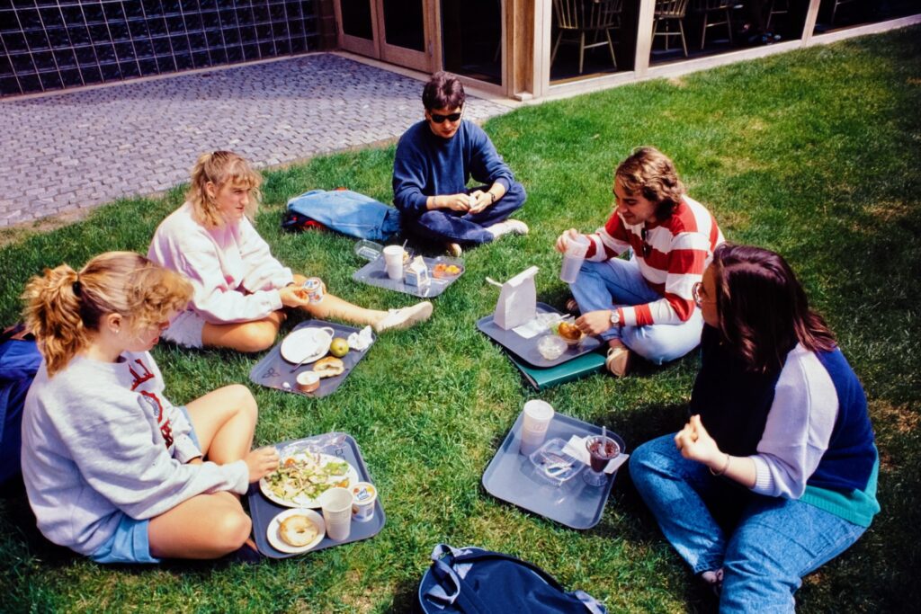five students eat lunch in the grass on trays outside Trillium Dining in spring 1992
