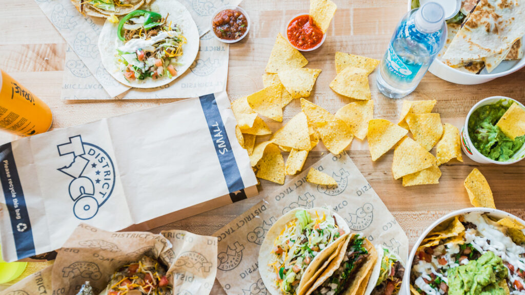 a product photo showing many of District Taco's offerings, from tacos and bowls to chips, salsas, and more