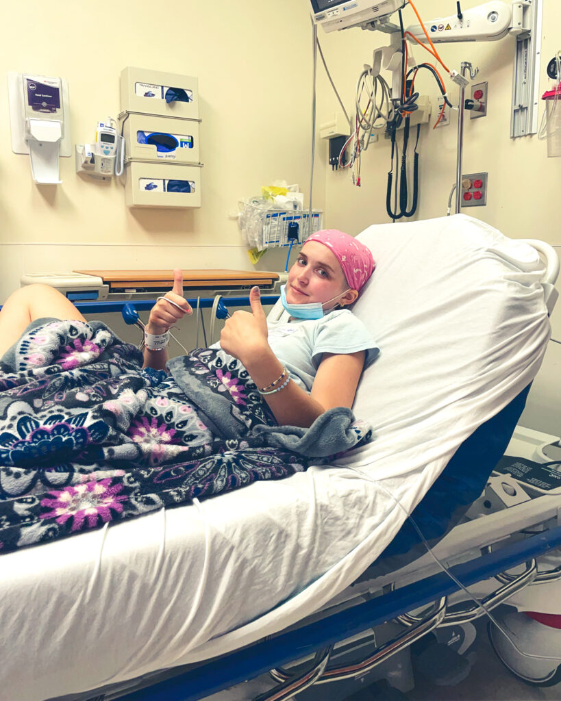 Camille Brady in a hospital bed giving a thumbs-up sign