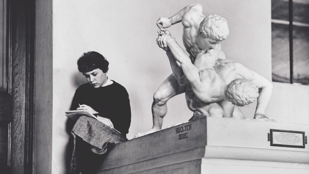 An undated black and white photo of a student studying while perched on one of the University's plaster cast collection items