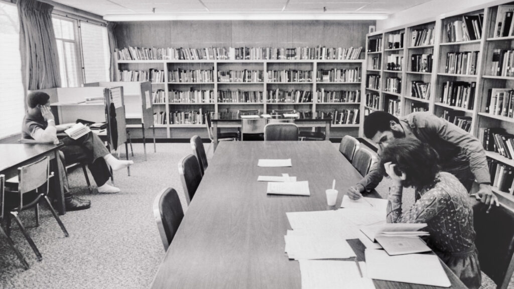An undated black and white photo of two students looking at a paper together in the Africana Studies and Research Center Library