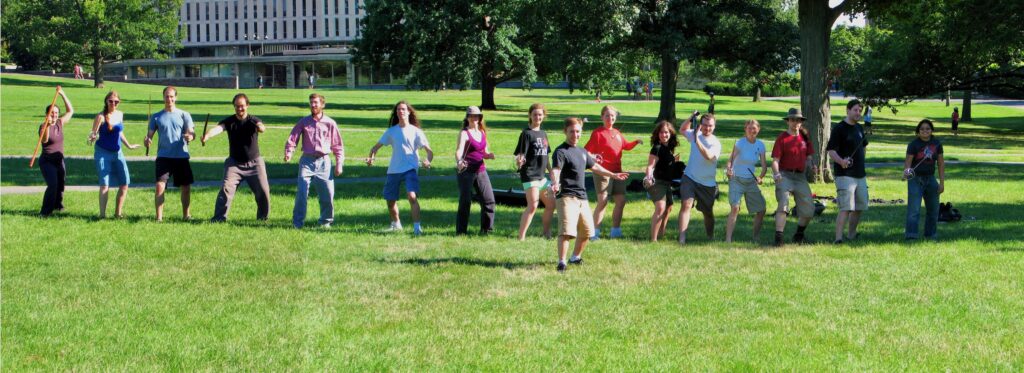 Jacob Lehman stands in front of a line of students, all holding swords outside.