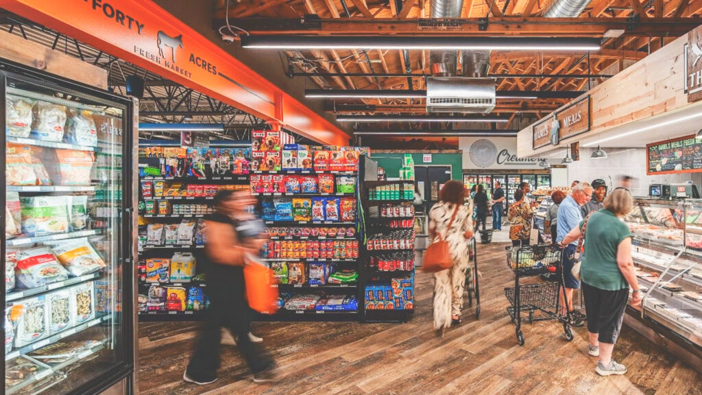 The back of the store at Forty Acres Fresh Market, featuring a deli counter with people in line, frozen foods, and aisles of other foods.