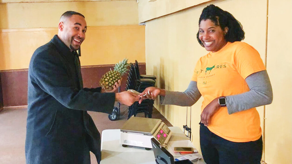 Elizabeth Abunaw smiles and shakes hands with a man who is buying a pineapple from her at her first pop-up market.