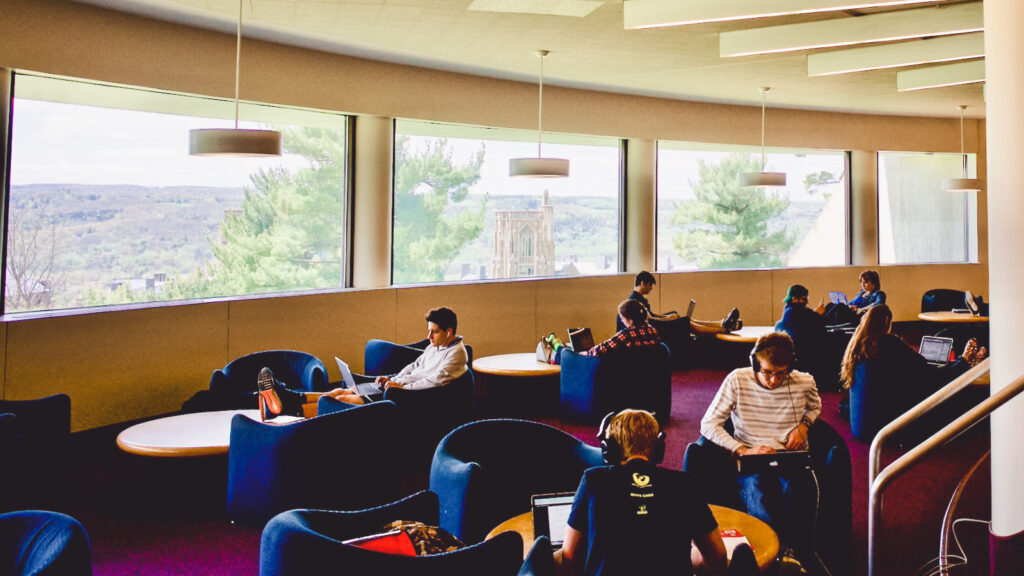 Students sit in blue chairs with their laptops while studying in the Uris Library Cocktail Lounge