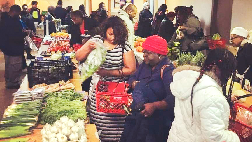 Dozens of customers scan tables of produce at a pop-up market.