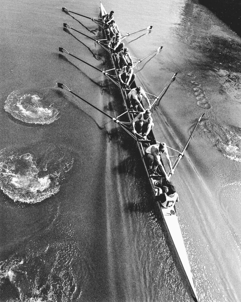 A black and white photo of a boat with athletes from the 1991 team, including Kennett, in action rowing.