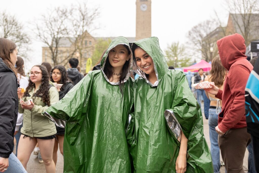 Two female students in green ponchos on Ho Plaza