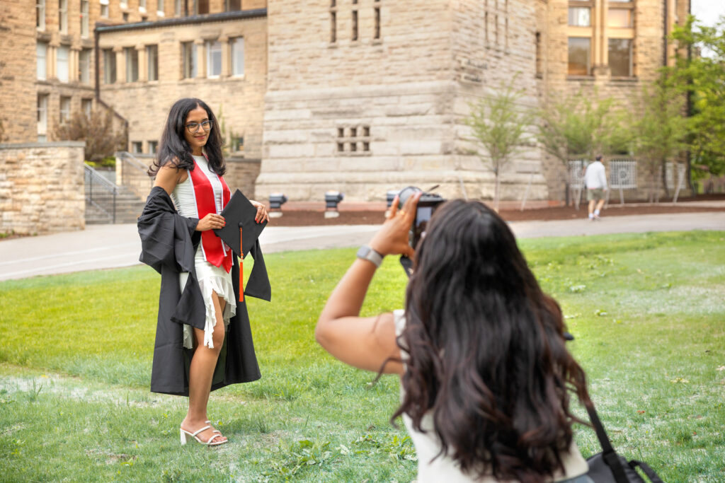 A student in her black graduation gown and stole poses for a photo on campus with her cap in hand.