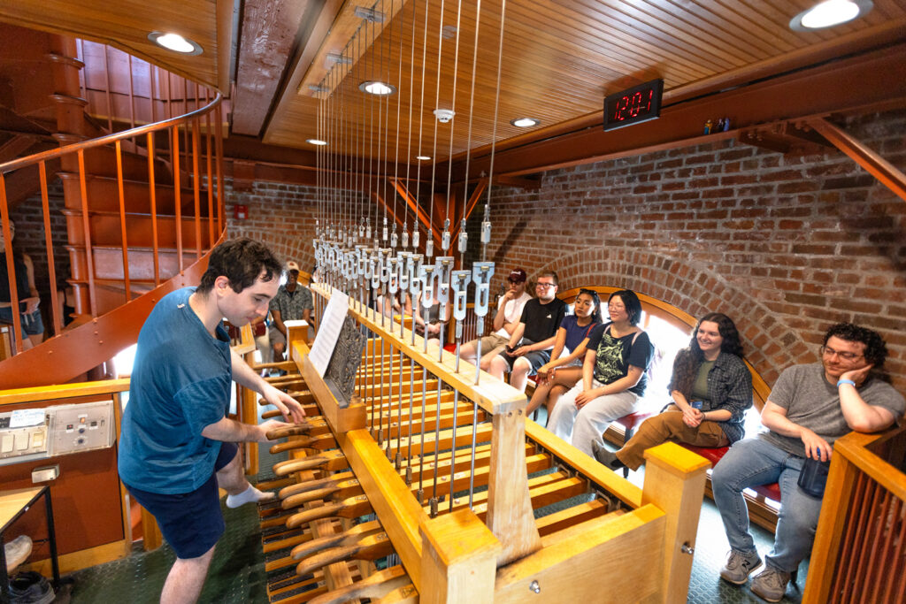 Chimesmasters give a chimes concert in McGraw Tower during Senior Week as people sit in front of the chimes and watch the performance.