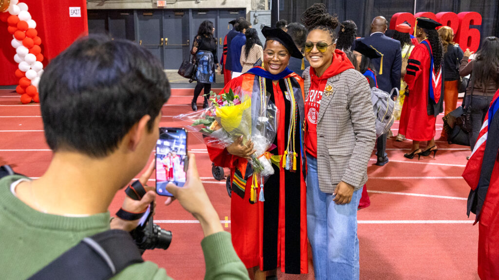 A woman in a PhD robe and a supporter get their photo taken in Barton Hall