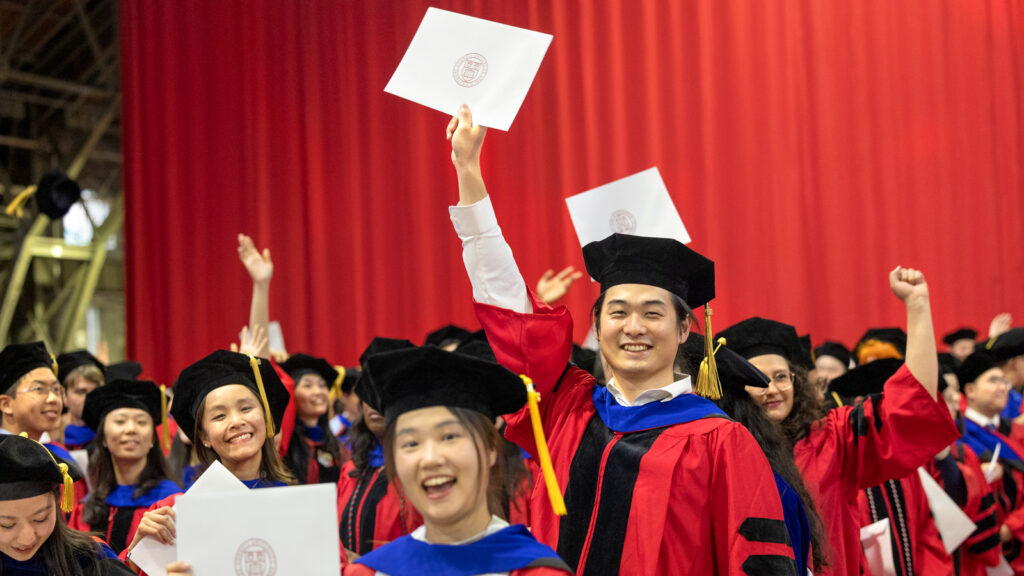 PhD grads celebrate as one man holds up his certificate