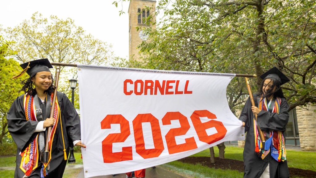 Grads carrying a banner that says Cornell 2026