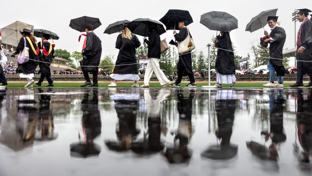 The grad procession carrying umbrellas and reflected in the wet pavement