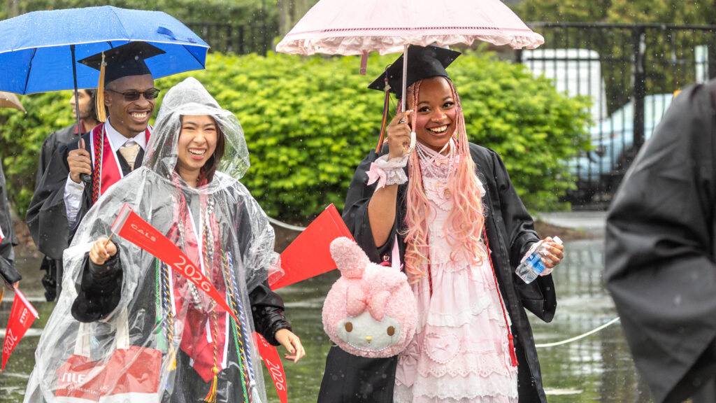 A grad in the procession has a pink umbrella, dress, and purse shaped like an anime character