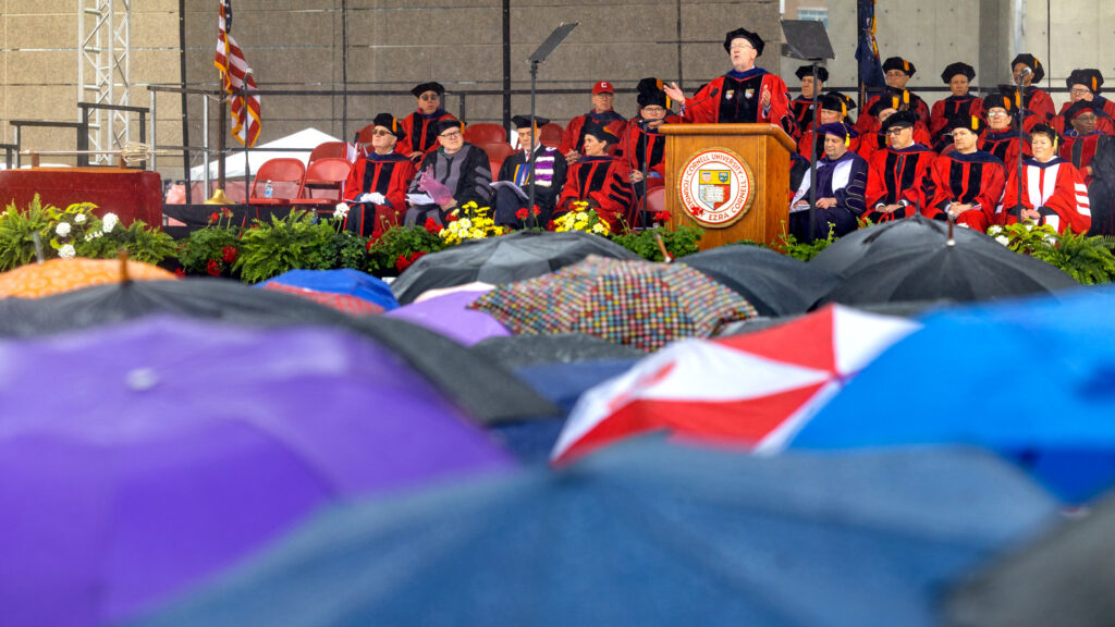 President Mike Kotlikoff at the podium onstage, with a sea of umbrellas in the foreground