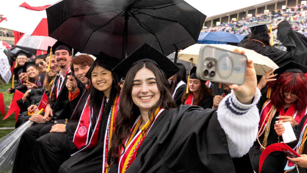 A row of students takes a selfie while seated at Commencement