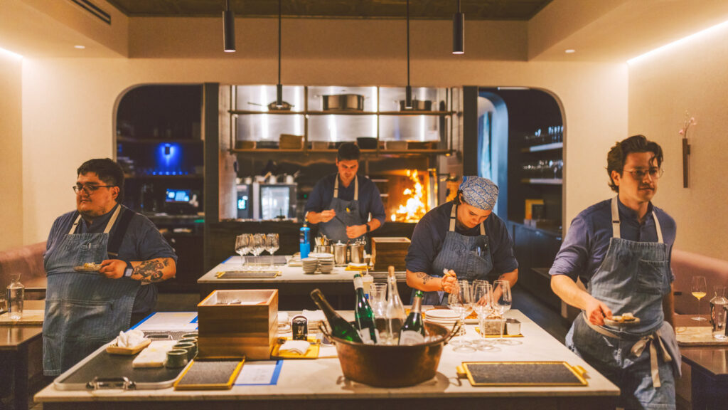 Jake Potashnick and three chefs plating courses and walking them to guest tables in the dining room.