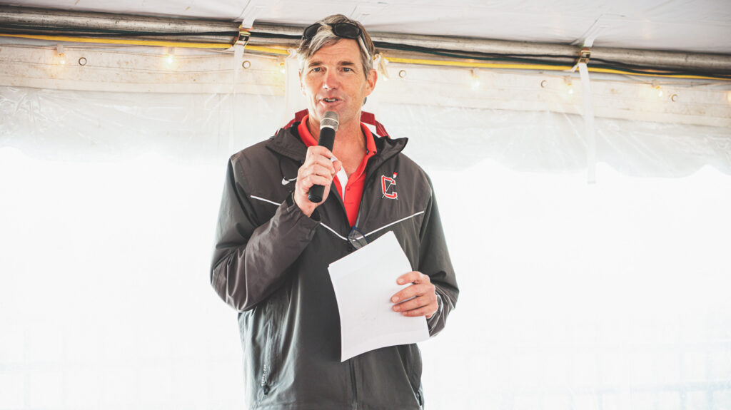 Todd Kennett holds a microphone and speaks at an event to celebrate 150 years of Cornell Rowing in 2022.