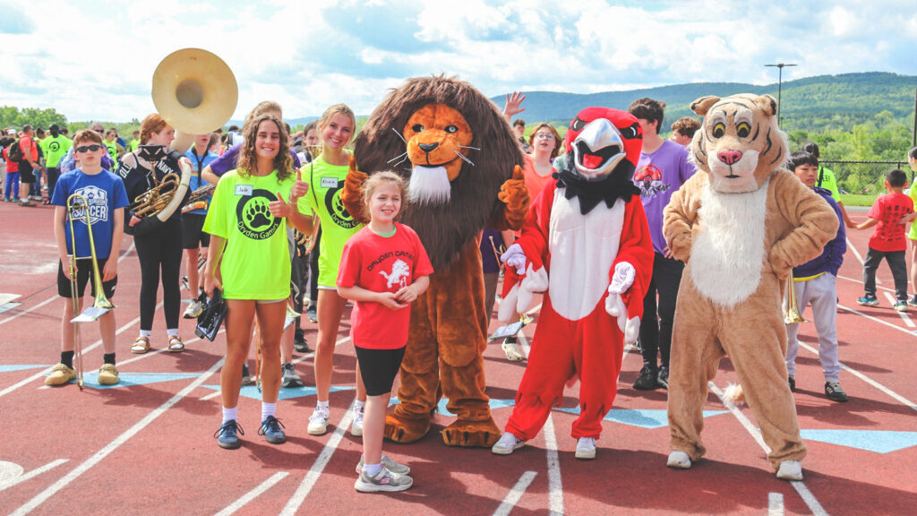 Three high school mascots (a lion, a tiger, and a red bird) on a running track with children