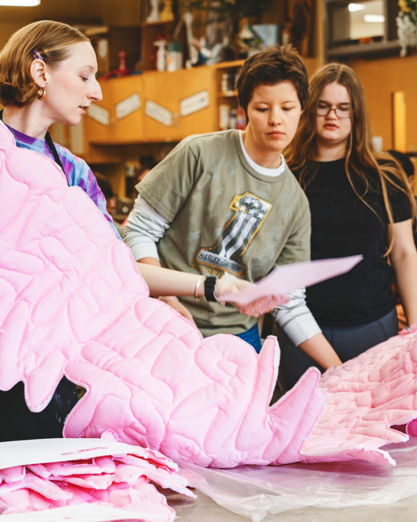 Anna Warfield and two high school students inspect the pink fabric in a classroom.
