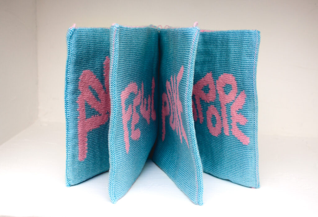 A blue fabric book with pink wording on the pages.