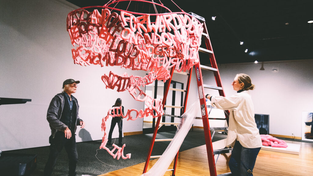 Anna Warfield climbs a ladder as she takes down her hanging installation in a museum.