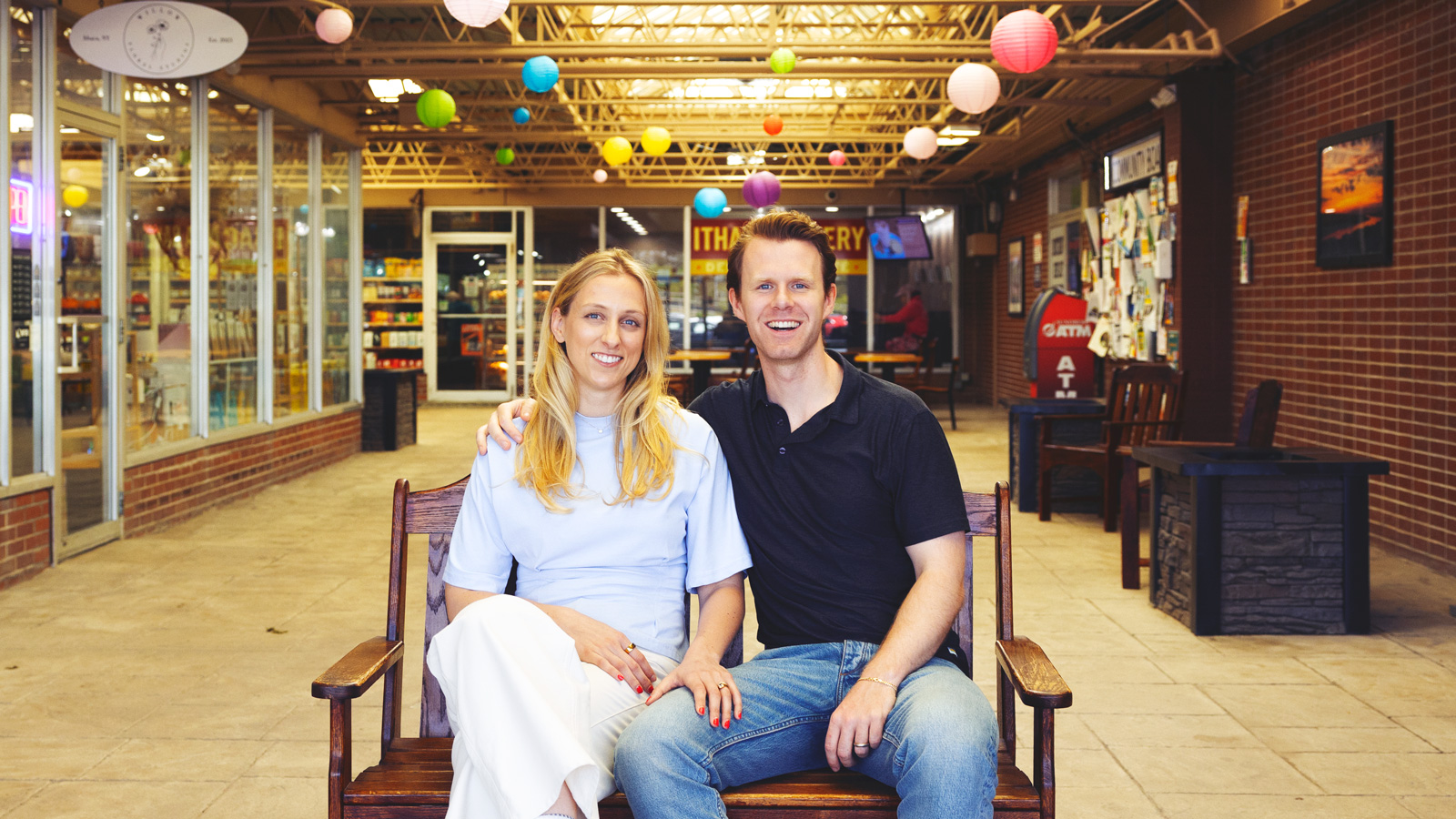 Spencer Kopko and Kristen Ferguson Kopko sitting on a bench together smiling inside the Triphammer Mall.