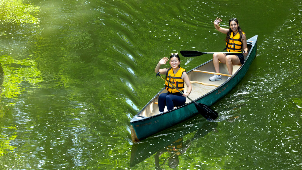 Two alumni smile and wave for a photo while canoeing on Beebe Lake at Reunion 2026