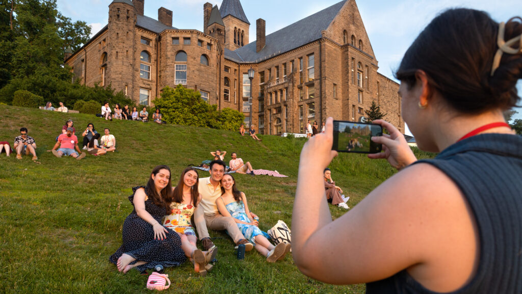 Four alumni pose for a photo as they sit on the Slope and watch the sunset during Reunion 2026
