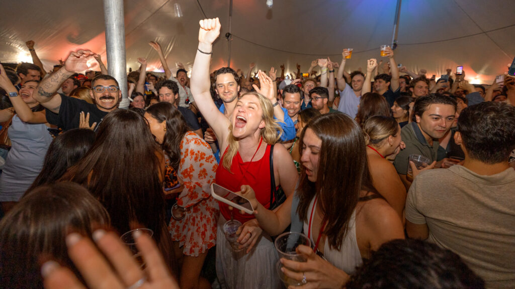 A crowd of people at a tent party on the Arts Quad dance and sing together at Reunion 2026