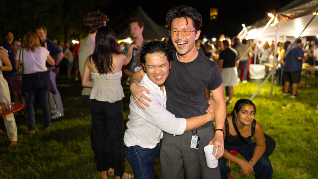 Two friends hug each other and smile for a photo at night at the tent parties on the Arts Quad at Reunion 2026
