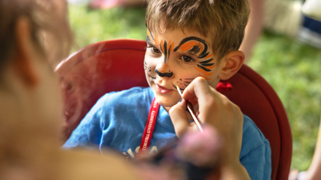 A boy gets his face painted like a lion during an event on the Arts Quad during Reunion 2026