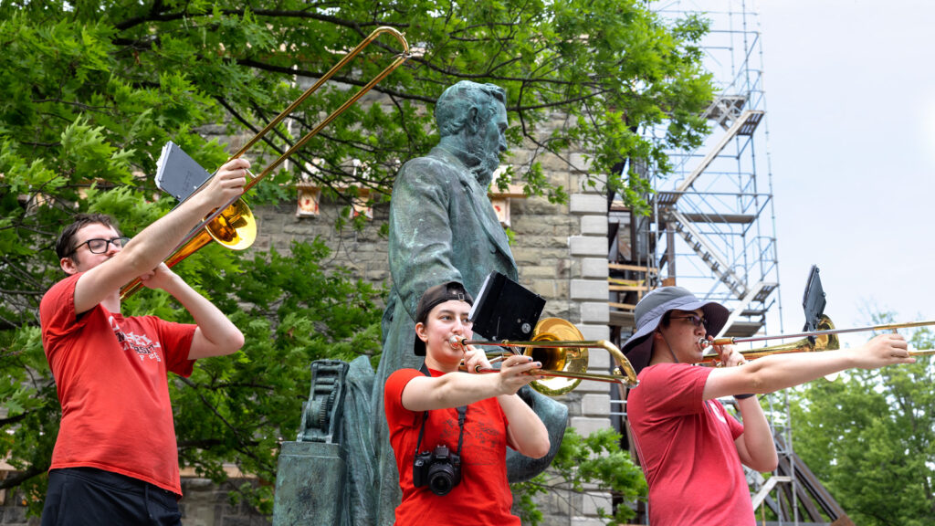 Three members of the Cornell Big Red Band play the trombone alongside the Arts Quad and the statue of Ezra Cornell during Reunion 2026