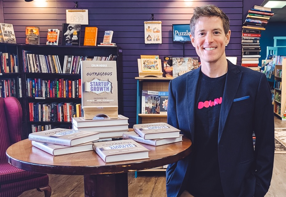 Colin Hodge standing in a bookstore next to a table holding stacks of his book