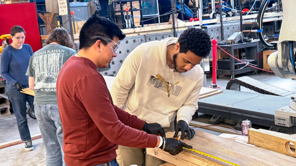 Two students in the Engineering in the Community course measure wood in a workshop