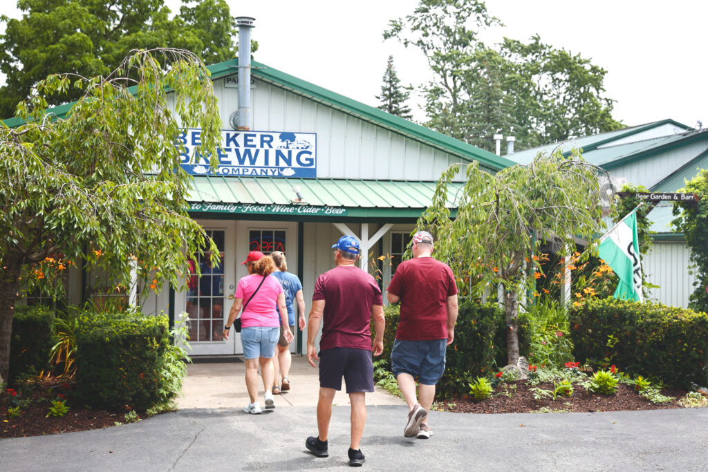 Four visitors walk into the brew pup entryway, which features flower beds, bushes, and small trees.
