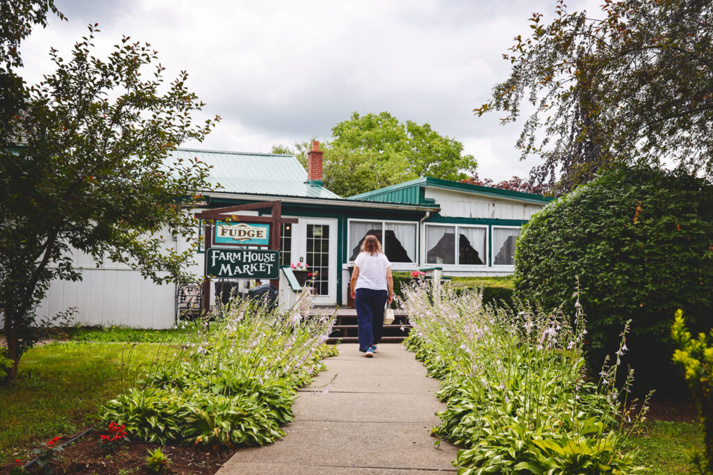 A visitor walks up the pathway featuring flowers on each side to the farm house market.