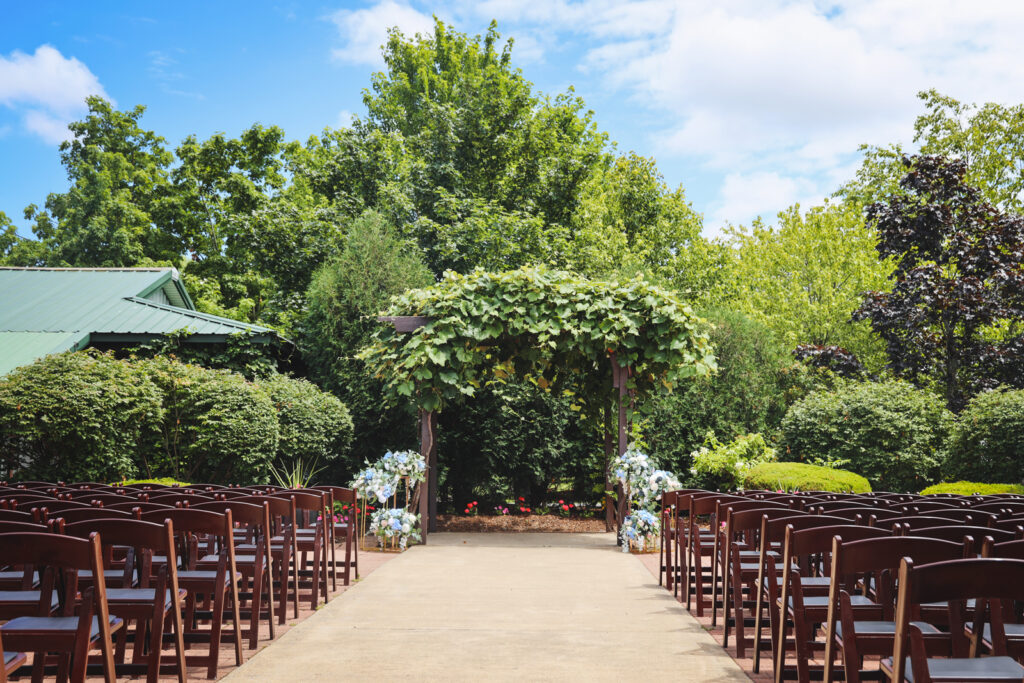 A wedding venue set up with rows of wooden chairs and an arch with white and blue flowers to the sides.