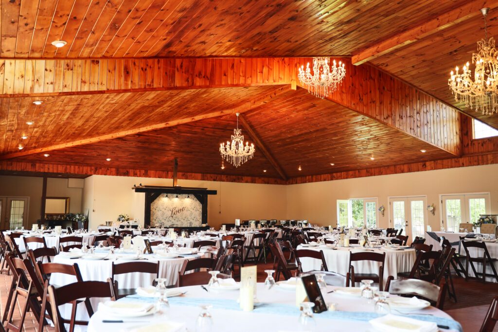 The inside of one of the pavilions at Becker Farms featuring chandeliers and tables with linens set up for a wedding.