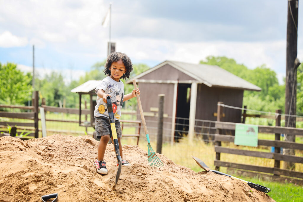 A child plays on a mound of sand with a shovel and rake in both hands at Becker Farms.
