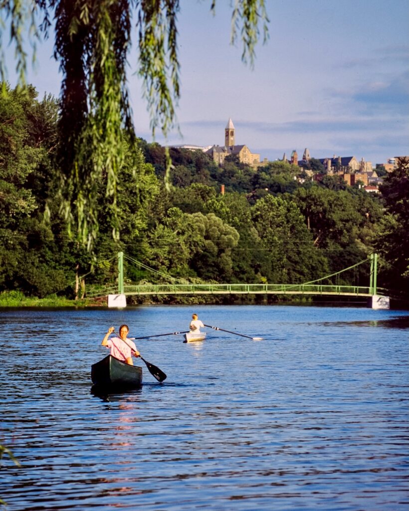 two Cornellians row on the inlet in Ithaca with McGraw Tower and campus buildings visible on the horizon far above them in a vintage color image from 1998