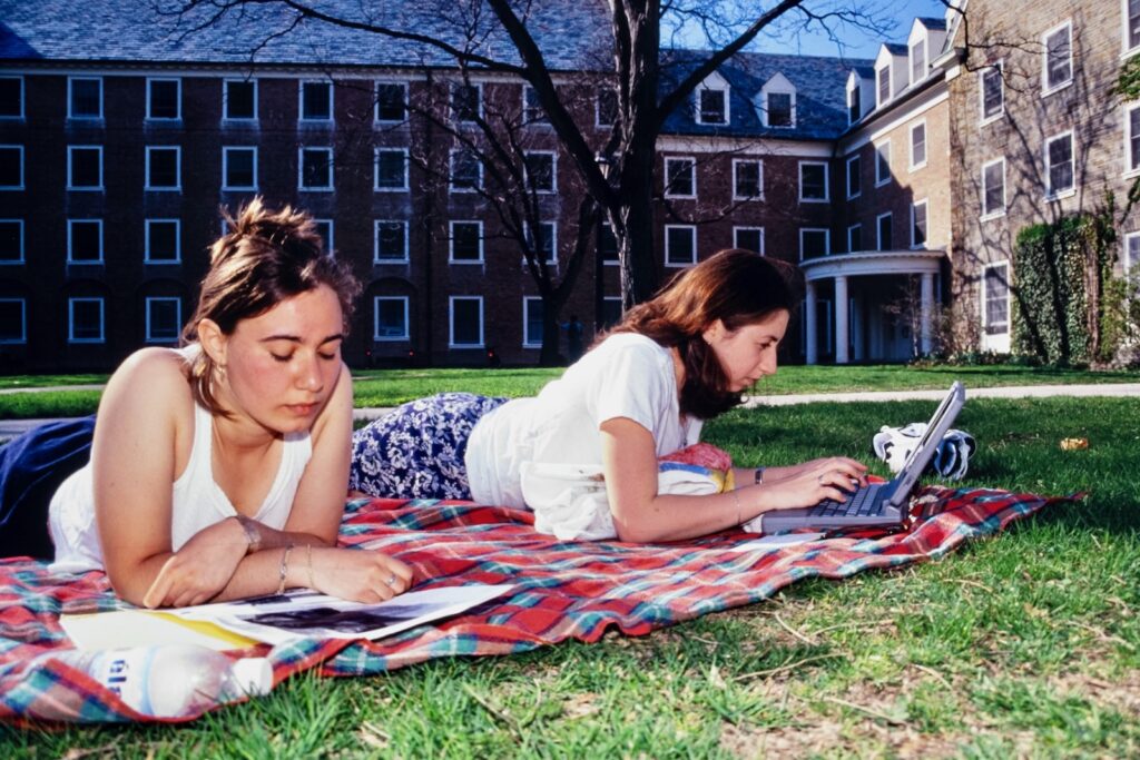 two students study on a blanket, one with a laptop, outside Dickson Hall in the 1990s